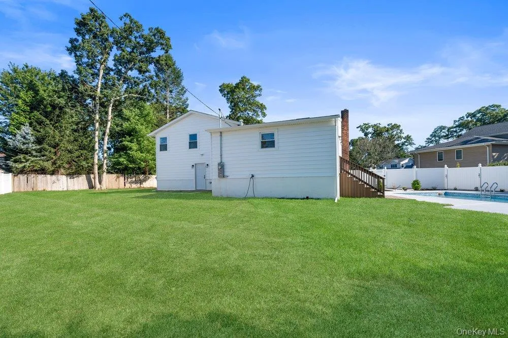 Expansive rear yard featuring a manicured lawn, an inground swimming pool, a wood privacy fence, and mature perimeter trees Expansive rear yard featuring a manicured lawn, an inground swimming pool, a wood privacy fence, and mature perimeter trees
