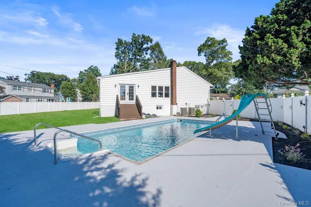 Fenced backyard featuring an in-ground swimming pool with an integrated slide, a concrete deck, and a manicured lawn Fenced backyard featuring an in-ground swimming pool with an integrated slide, a concrete deck, and a manicured lawn