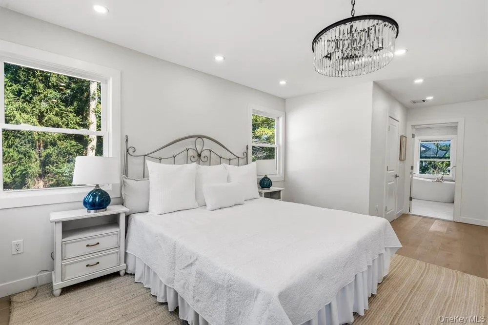 Primary Bedroom Featuring two windows, recessed lighting, European Oak flooring, decorative chandelier, and a partial view of The Primary Bath with a freestanding tub Primary Bedroom Featuring two windows, recessed lighting, European Oak flooring, decorative chandelier, and a partial view of The Primary Bath with a freestanding tub