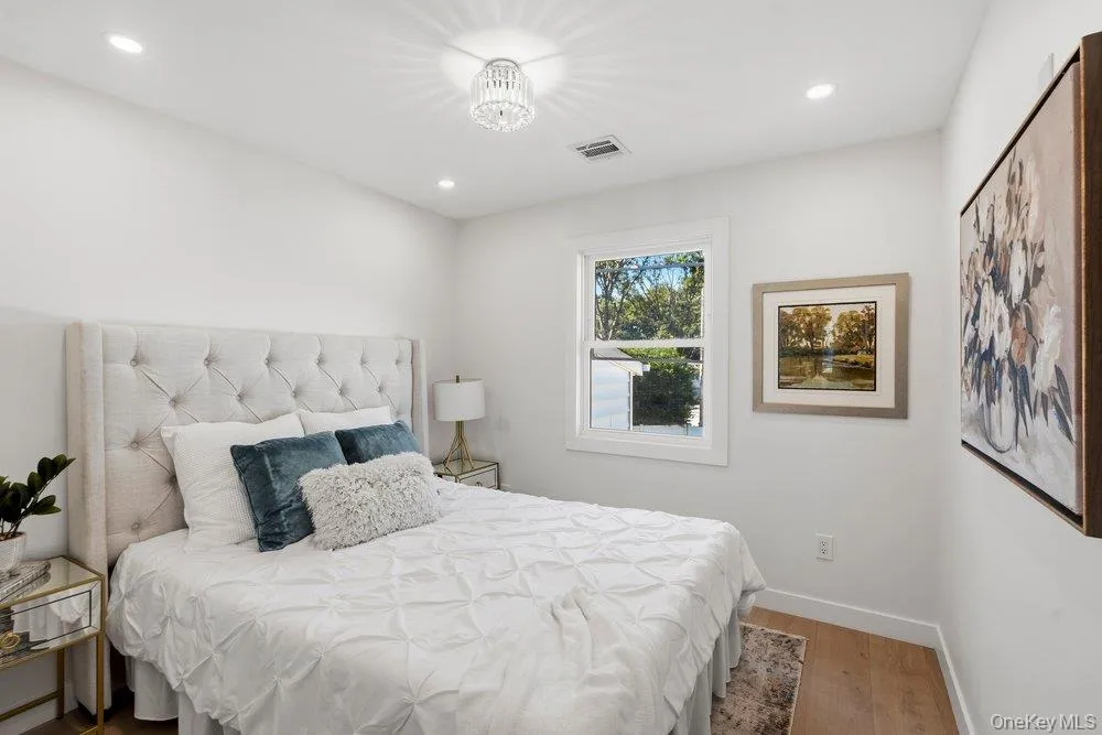 Bright bedroom with a double-pane window, recessed lighting, and a contemporary ceiling fixture Bright bedroom with a double-pane window, recessed lighting, and a contemporary ceiling fixture
