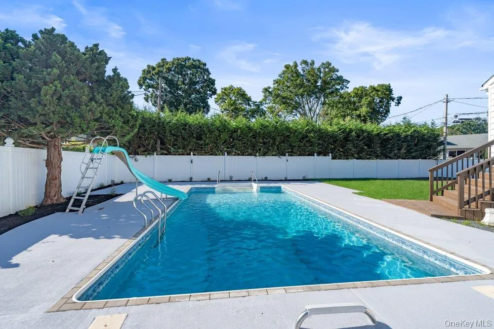 Spacious backyard featuring a rectangular in-ground pool with a blue tile border, a dedicated pool slide, and an expansive concrete patio Spacious backyard featuring a rectangular in-ground pool with a blue tile border, a dedicated pool slide, and an expansive concrete patio