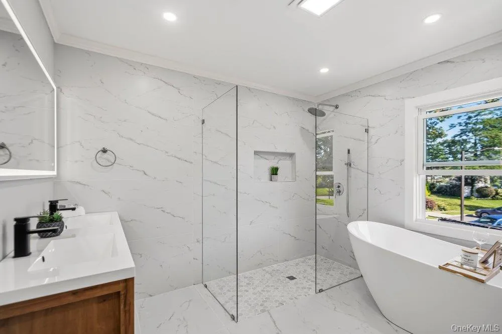 Primary Bath features a freestanding soaking tub, a frameless glass shower enclosure with a built-in niche, and large format wall and floor tiling Primary Bath features a freestanding soaking tub, a frameless glass shower enclosure with a built-in niche, and large format wall and floor tiling