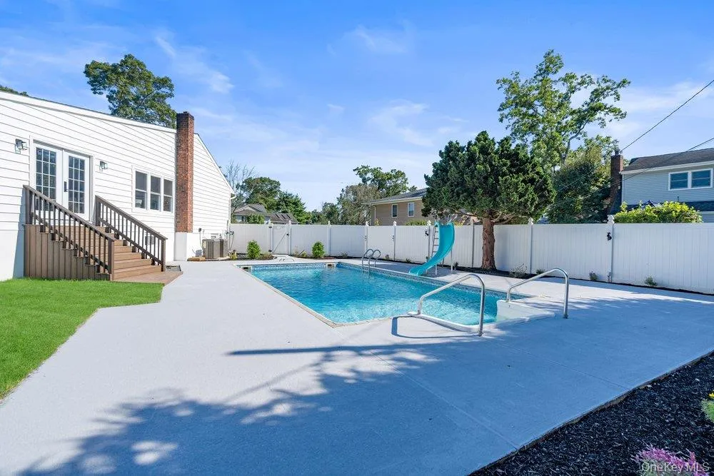 In-ground swimming pool with diving board and slip-resistant blue deck surface, complemented by manicured lawn, white vinyl fencing, mature shade trees, and a single-story residence with covered entry deck and brick chimney detail In-ground swimming pool with diving board and slip-resistant blue deck surface, complemented by manicured lawn, white vinyl fencing, mature shade trees, and a single-story residence with covered entry deck and brick chimney detail