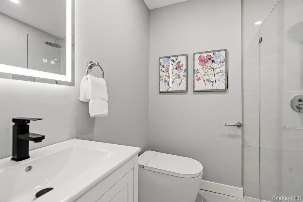 Modern bathroom featuring Contemporary vanity with an integrated sink, matte black faucet, and an illuminated mirror Modern bathroom featuring Contemporary vanity with an integrated sink, matte black faucet, and an illuminated mirror
