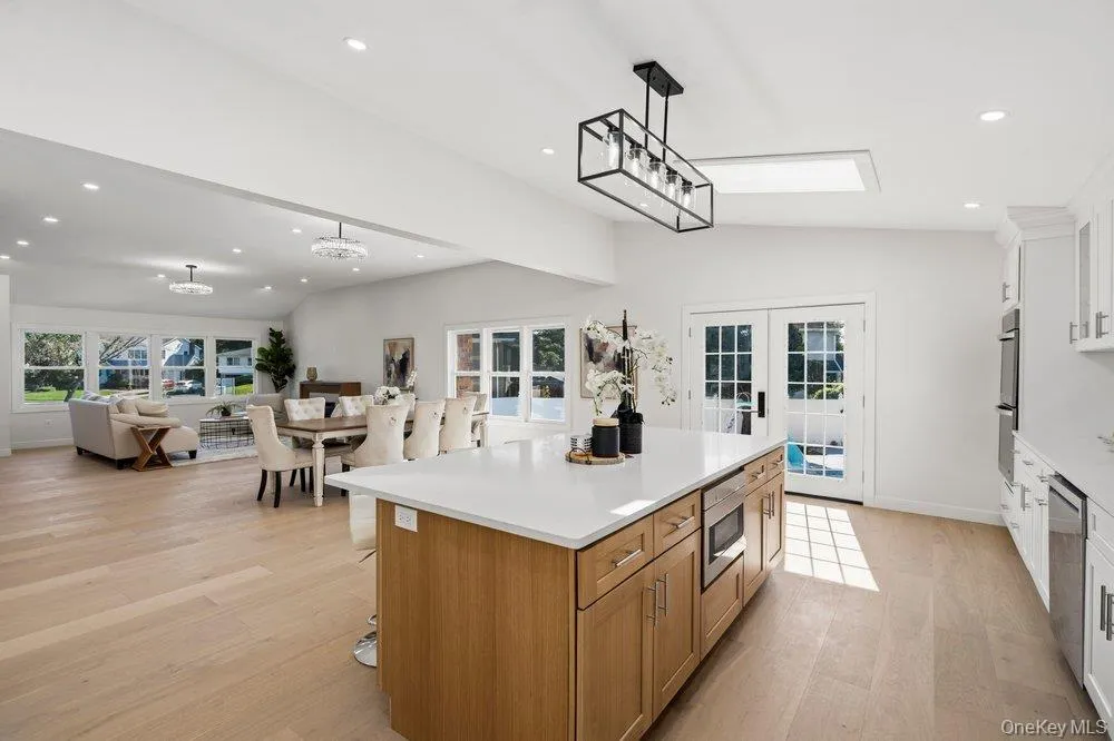 Spacious kitchen featuring a central island with integrated microwave, light wood-finish flooring, white cabinetry, and French patio doors with transom window Spacious kitchen featuring a central island with integrated microwave, light wood-finish flooring, white cabinetry, and French patio doors with transom window