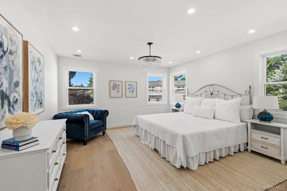 Spacious bedroom featuring light wood-finish flooring, recessed lighting, multiple windows, and a decorative chandelier Spacious bedroom featuring light wood-finish flooring, recessed lighting, multiple windows, and a decorative chandelier