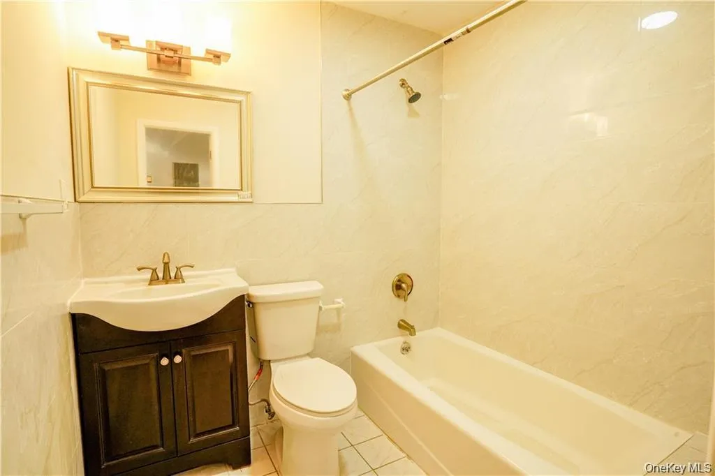 Elegantly appointed bathroom featuring a curved pedestal sink with brass hardware, wood-finish vanity cabinet, ceramic tile flooring, and a full soaking tub with glass enclosure and brass fixtures Elegantly appointed bathroom featuring a curved pedestal sink with brass hardware, wood-finish vanity cabinet, ceramic tile flooring, and a full soaking tub with glass enclosure and brass fixtures