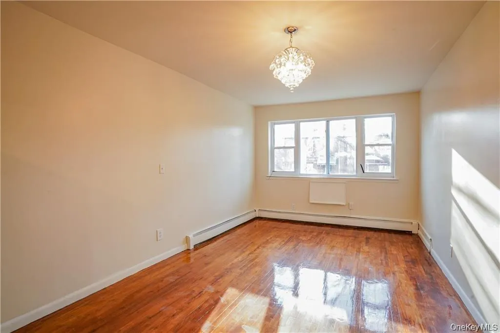 Room featuring a multi-pane window, wood-finish flooring, a crystal chandelier, and baseboard heating Room featuring a multi-pane window, wood-finish flooring, a crystal chandelier, and baseboard heating