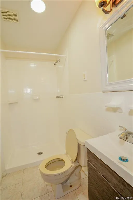 Bathroom featuring a shower stall, toilet, and vanity with an integrated sink Bathroom featuring a shower stall, toilet, and vanity with an integrated sink