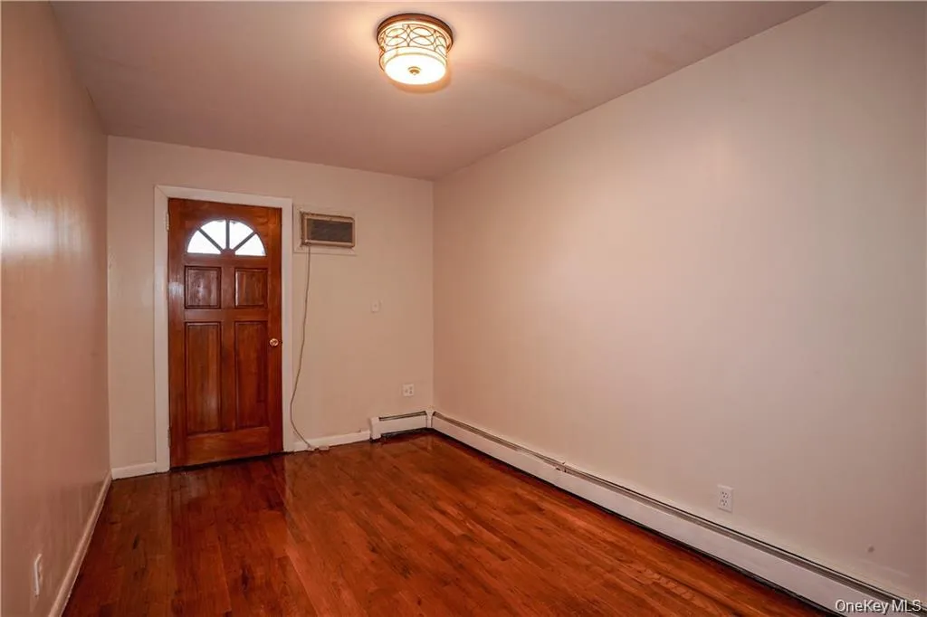 Entryway featuring a wood-finish door with an arched transom window, wood-finish flooring, and baseboard heating Entryway featuring a wood-finish door with an arched transom window, wood-finish flooring, and baseboard heating