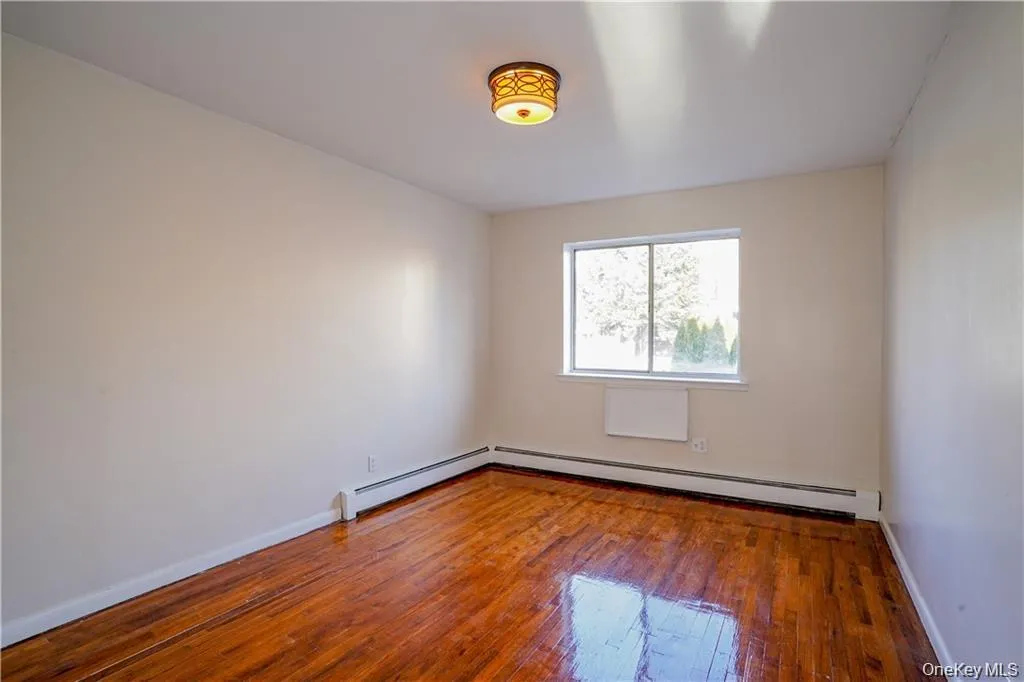 Room featuring wood-finish flooring, a double-pane window, and a decorative flush-mount ceiling light fixture Room featuring wood-finish flooring, a double-pane window, and a decorative flush-mount ceiling light fixture