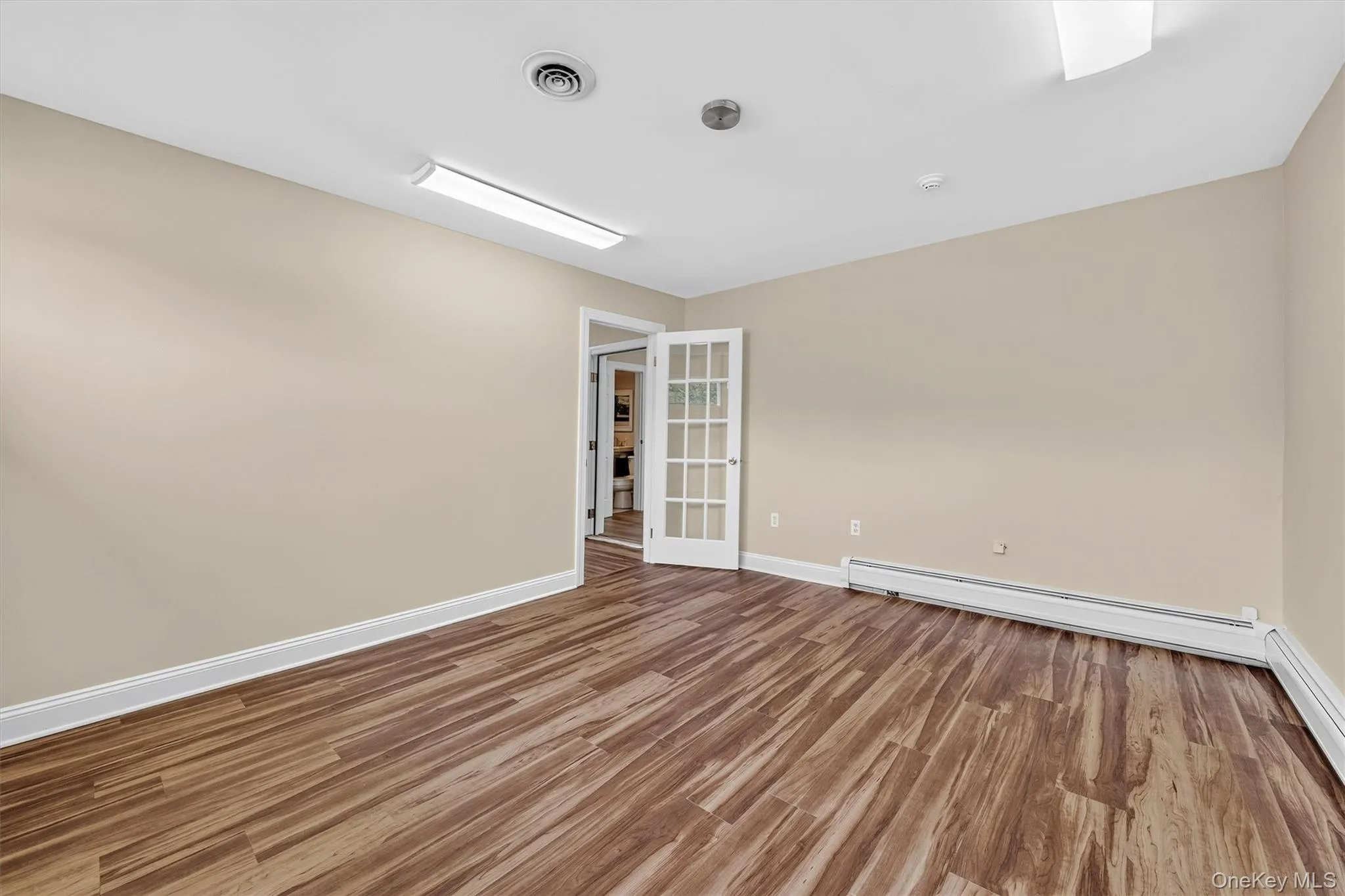 Wood-finish flooring, neutral wall tones, white trim, and a full-light French door with white framing Wood-finish flooring, neutral wall tones, white trim, and a full-light French door with white framing