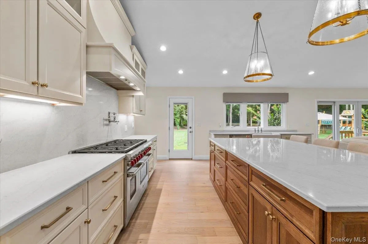 Gourmet kitchen featuring a large central island, light-toned cabinetry, stainless steel range, and light wood-finish flooring Gourmet kitchen featuring a large central island, light-toned cabinetry, stainless steel range, and light wood-finish flooring