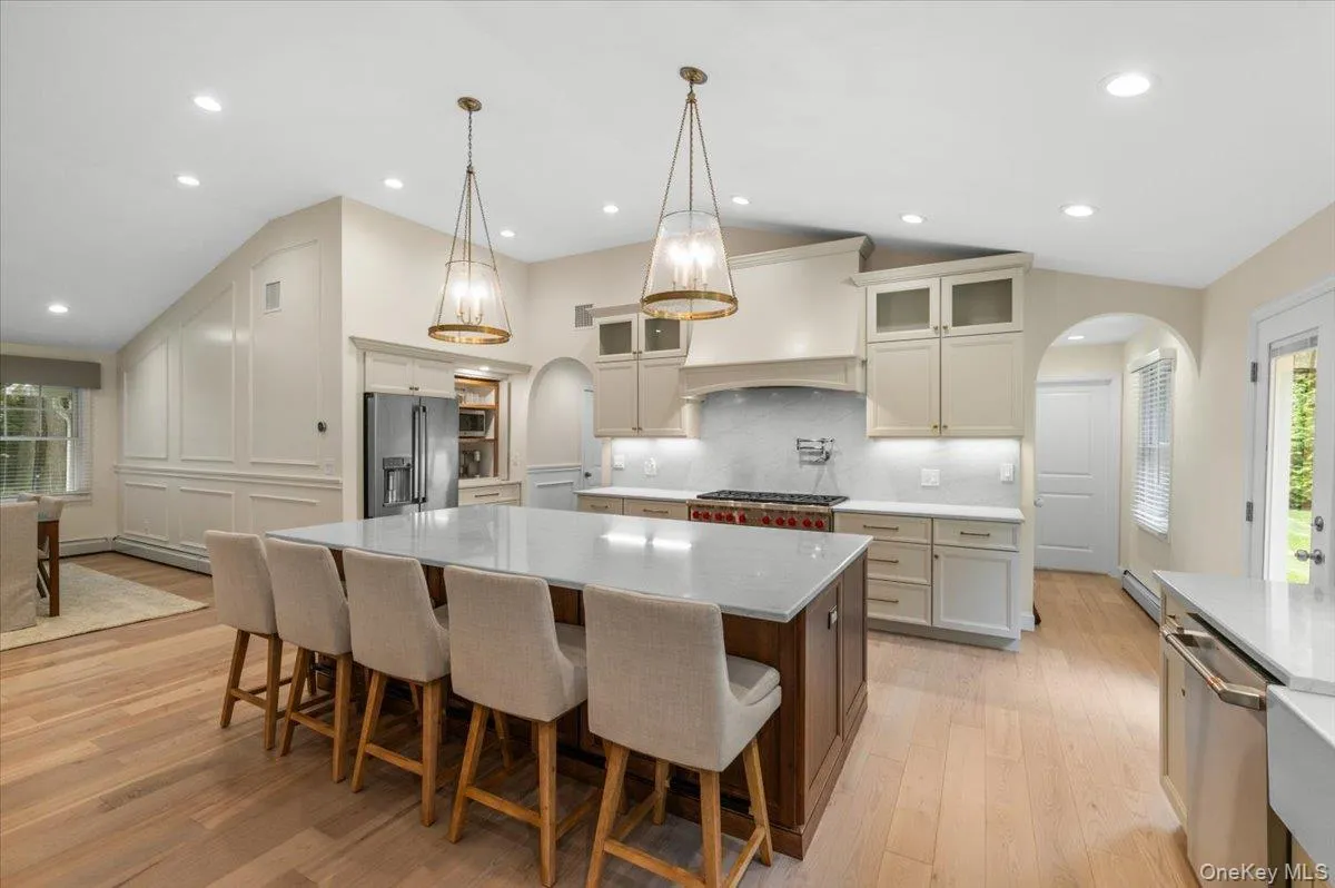 Spacious kitchen featuring a large central island with seating, light wood-finish flooring, recessed lighting, and a vaulted ceiling Spacious kitchen featuring a large central island with seating, light wood-finish flooring, recessed lighting, and a vaulted ceiling