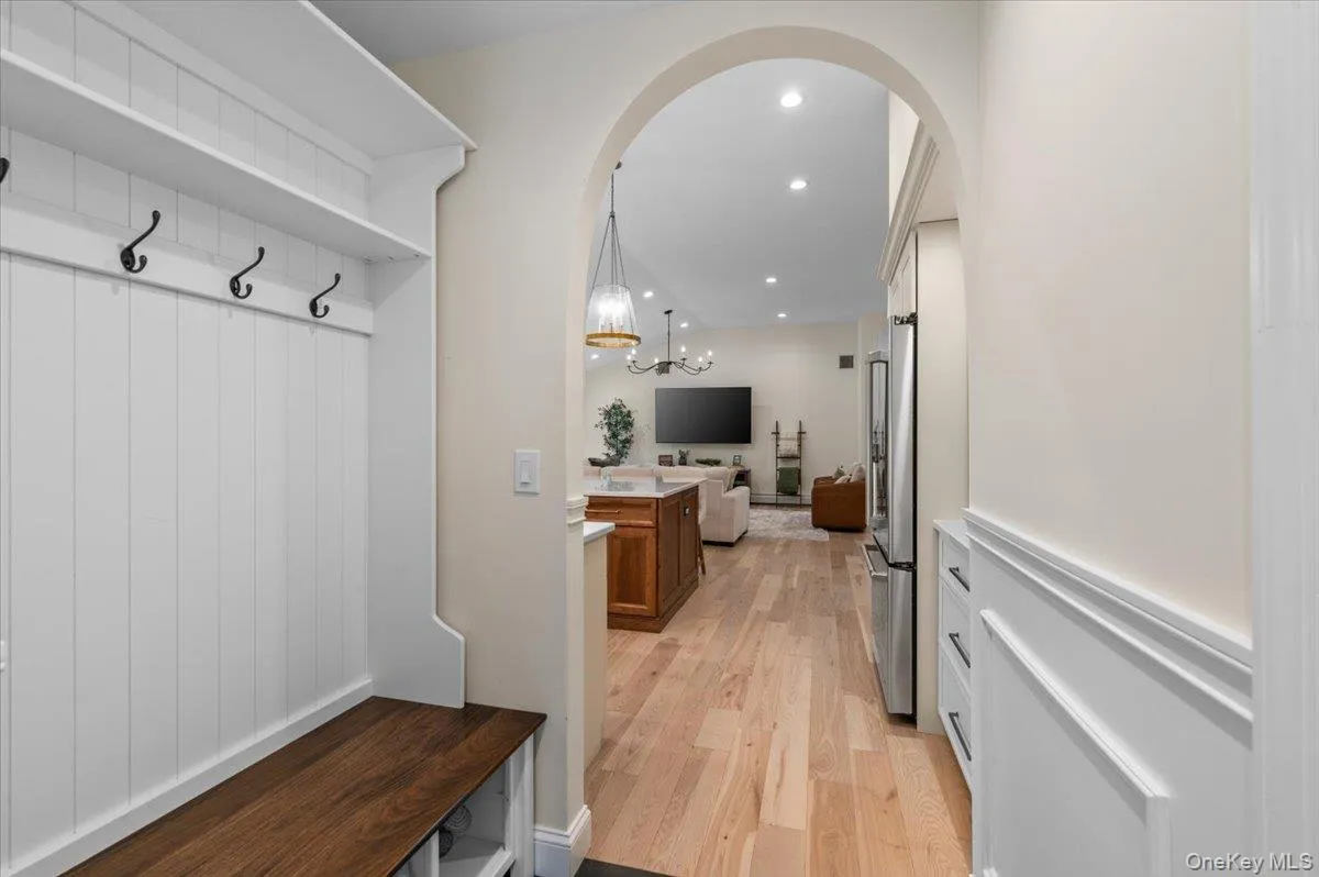 Built-in mudroom bench with storage, arched doorway, wood-finish flooring, recessed lighting, and stainless steel refrigerator Built-in mudroom bench with storage, arched doorway, wood-finish flooring, recessed lighting, and stainless steel refrigerator