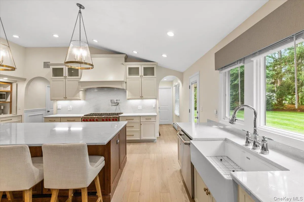 Spacious kitchen featuring a large central island, light wood-finish flooring, recessed lighting, and a farmhouse sink Spacious kitchen featuring a large central island, light wood-finish flooring, recessed lighting, and a farmhouse sink