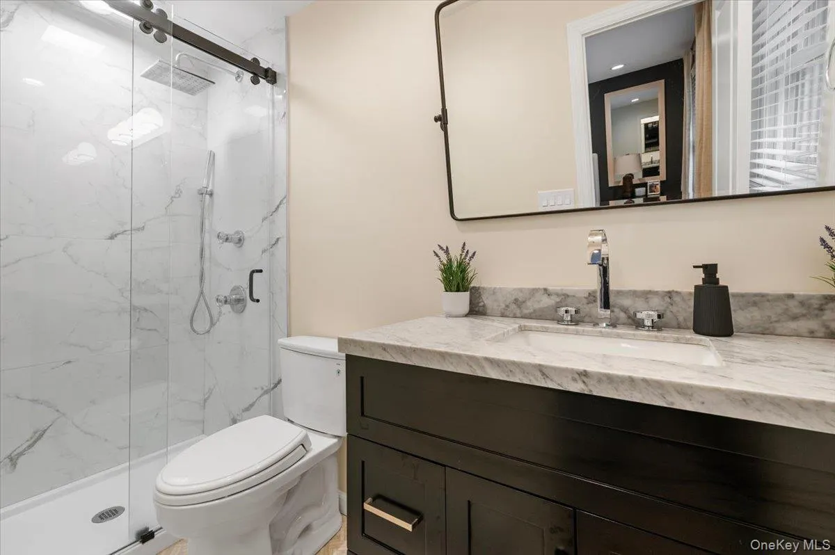 Tiled shower with sliding glass door, dark wood-finish vanity, integrated sink, and stone countertop Tiled shower with sliding glass door, dark wood-finish vanity, integrated sink, and stone countertop