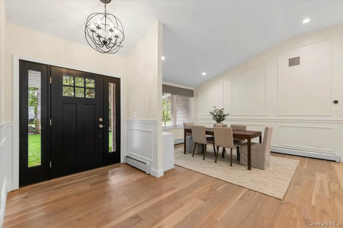 Black paneled entry door with sidelights, wood-finish flooring, and a contemporary spherical chandelier Black paneled entry door with sidelights, wood-finish flooring, and a contemporary spherical chandelier