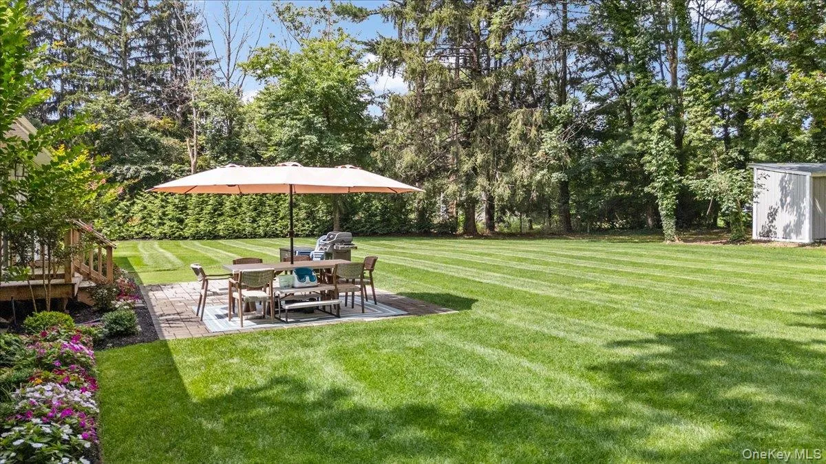 Expansive backyard featuring a manicured lawn, paver patio, established landscaping, and mature trees Expansive backyard featuring a manicured lawn, paver patio, established landscaping, and mature trees