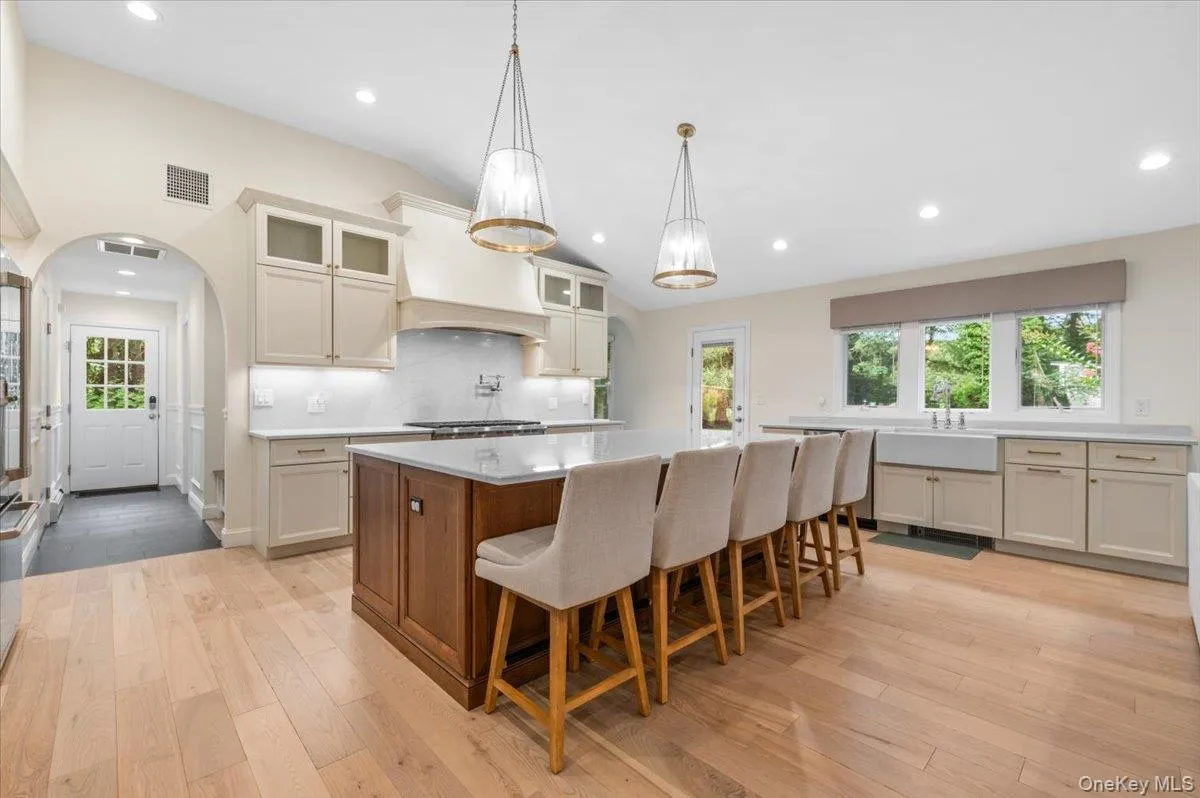 Spacious kitchen featuring an expansive center island, light wood-finish flooring, white apron-front sink, and custom cabinetry with under-cabinet lighting Spacious kitchen featuring an expansive center island, light wood-finish flooring, white apron-front sink, and custom cabinetry with under-cabinet lighting