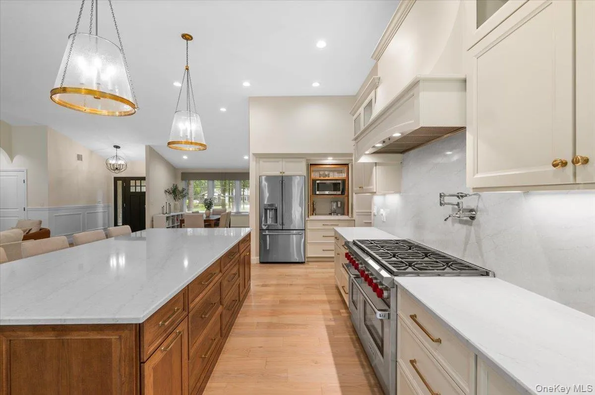 Gourmet kitchen featuring a substantial island with stone countertop, wood-finish base cabinetry, stainless steel appliances, a professional-grade range, and overhead pendant lighting Gourmet kitchen featuring a substantial island with stone countertop, wood-finish base cabinetry, stainless steel appliances, a professional-grade range, and overhead pendant lighting