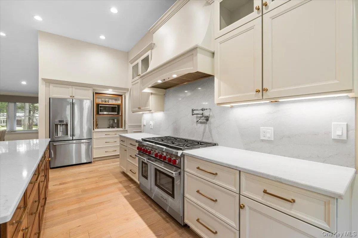 Stainless steel range with a pot filler, light wood-finish flooring, white upper and lower cabinetry, white countertops, and integrated stainless steel appliances Stainless steel range with a pot filler, light wood-finish flooring, white upper and lower cabinetry, white countertops, and integrated stainless steel appliances