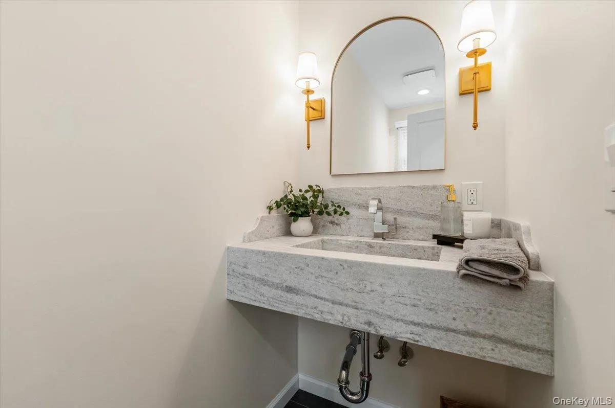 Floating vanity with integrated basin, polished chrome faucet, arched mirror, and brass-finish wall sconces Floating vanity with integrated basin, polished chrome faucet, arched mirror, and brass-finish wall sconces