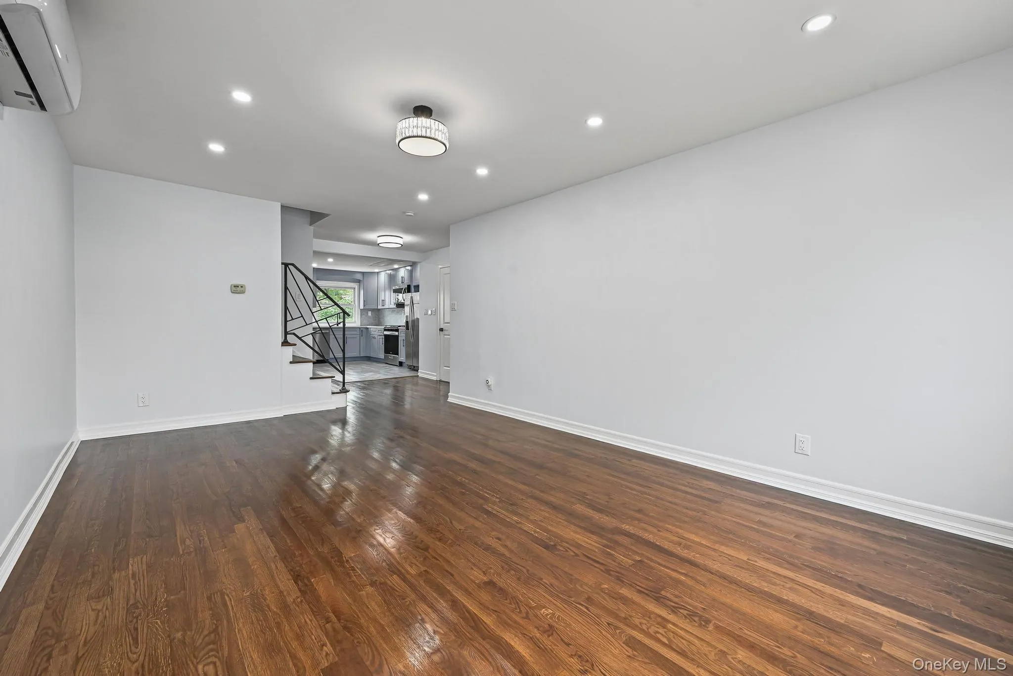 Unfurnished living room with recessed lighting, a wall unit AC, dark wood-style flooring, and stairs Unfurnished living room with recessed lighting, a wall unit AC, dark wood-style flooring, and stairs