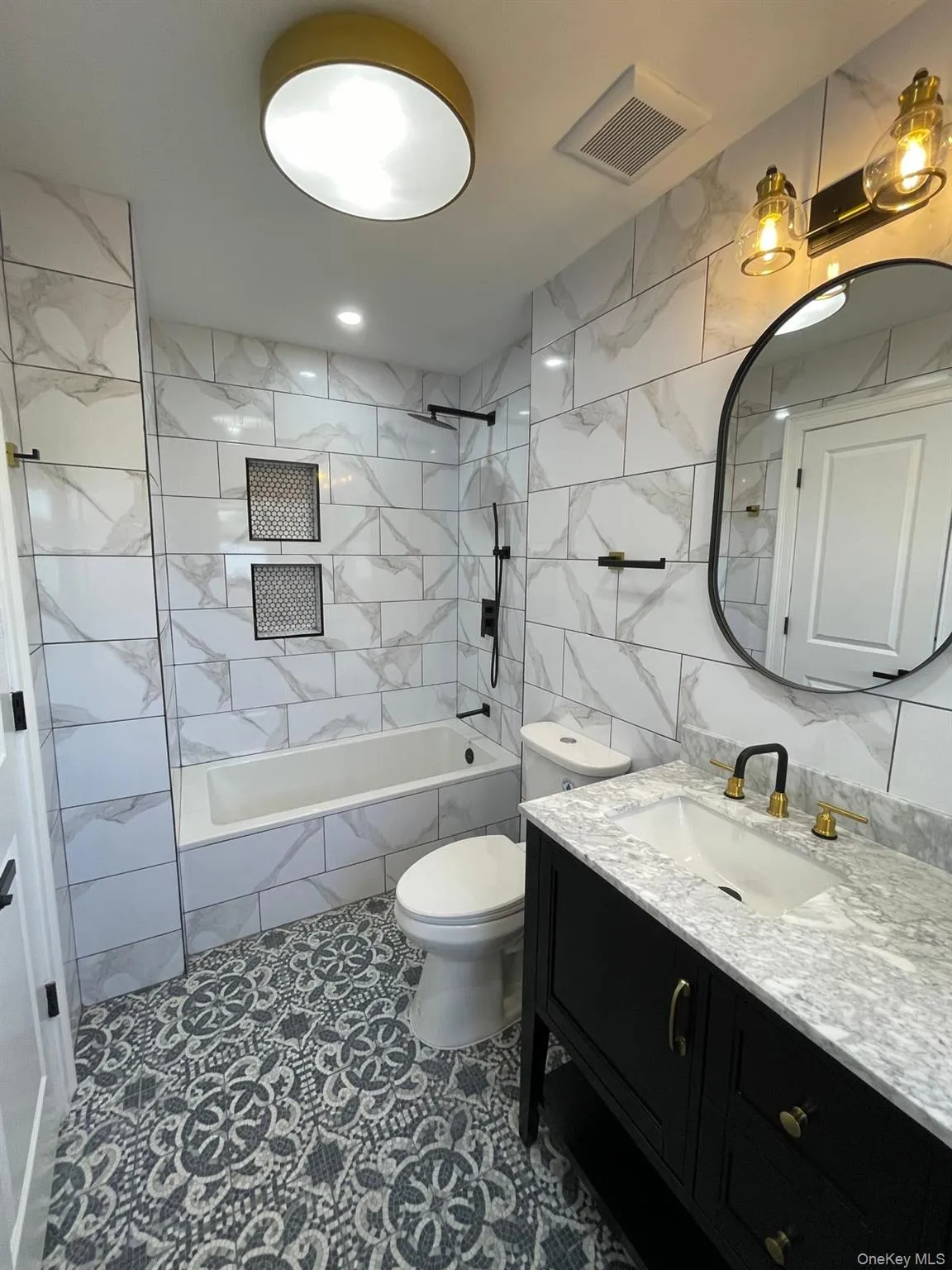 Full bathroom with tile walls, vanity, tiled shower / bath, and dark tile patterned floors Full bathroom with tile walls, vanity, tiled shower / bath, and dark tile patterned floors