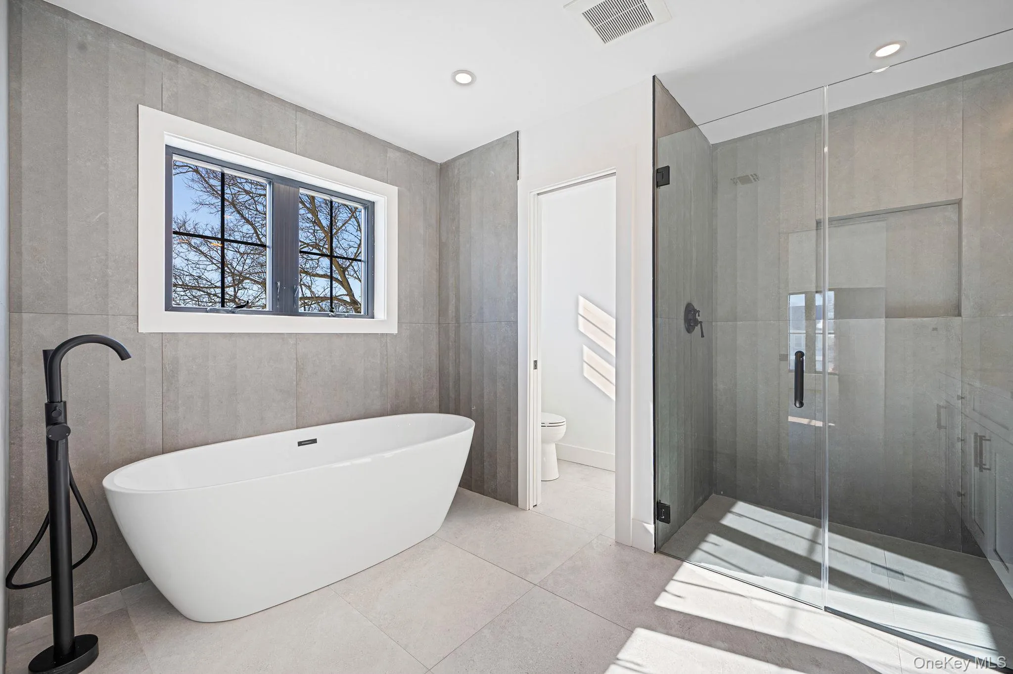 Spa like primary bath featuring a freestanding soaking tub, oversized glass shower, and modern finishes. Spa like primary bath featuring a freestanding soaking tub, oversized glass shower, and modern finishes.