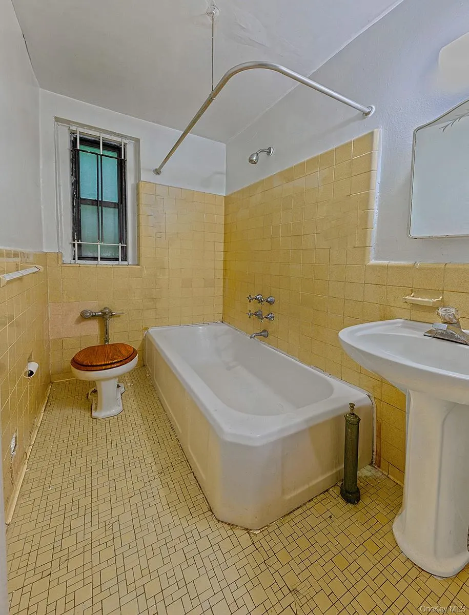 Bathroom featuring a pedestal sink, white bathtub, and yellow wall tiling Bathroom featuring a pedestal sink, white bathtub, and yellow wall tiling