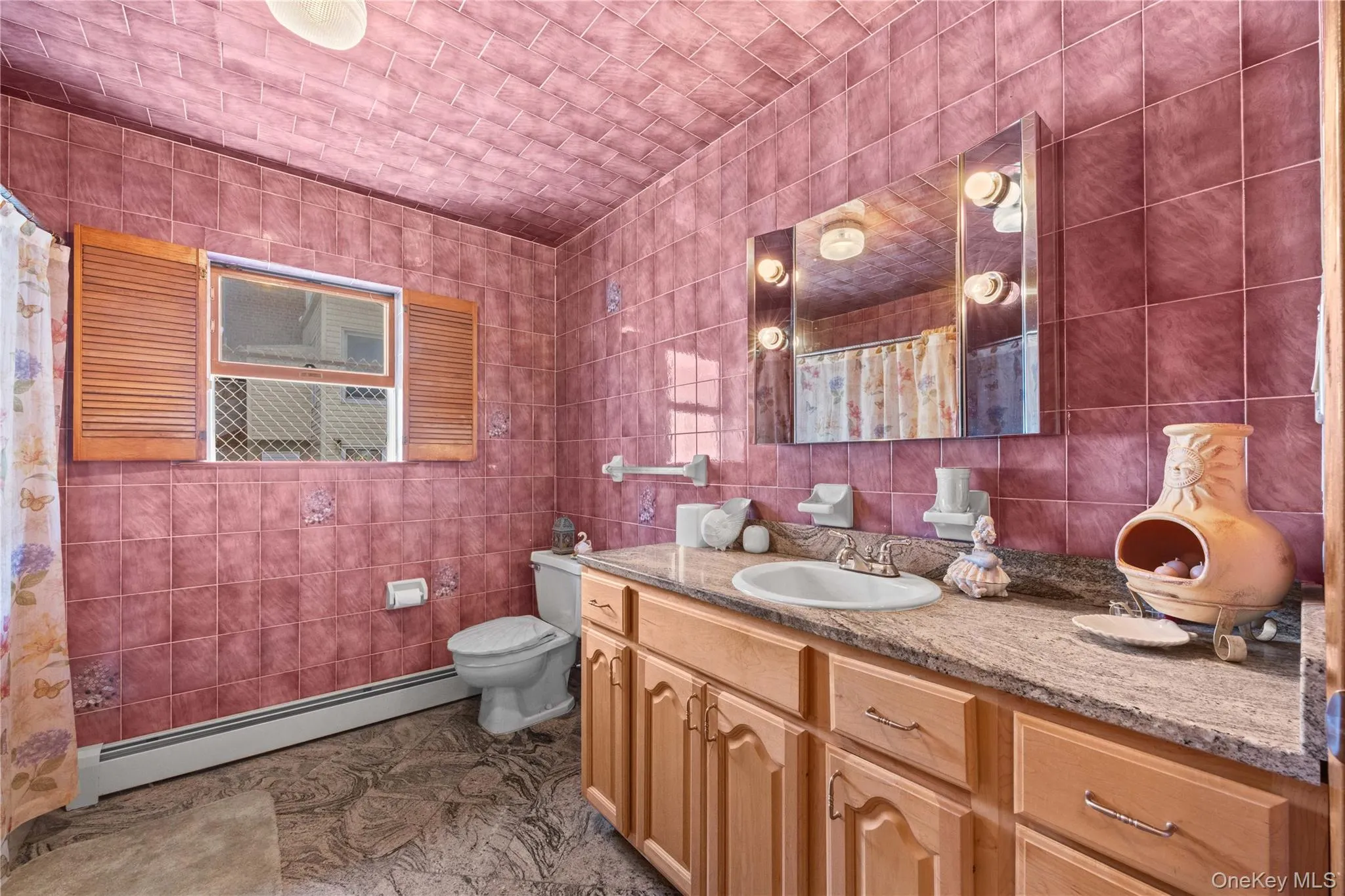 Bathroom featuring full wall and ceiling tiling, a wood-finish vanity with a built-in sink, a stone-finish countertop, and a mirrored medicine cabinet with integrated lighting Bathroom featuring full wall and ceiling tiling, a wood-finish vanity with a built-in sink, a stone-finish countertop, and a mirrored medicine cabinet with integrated lighting