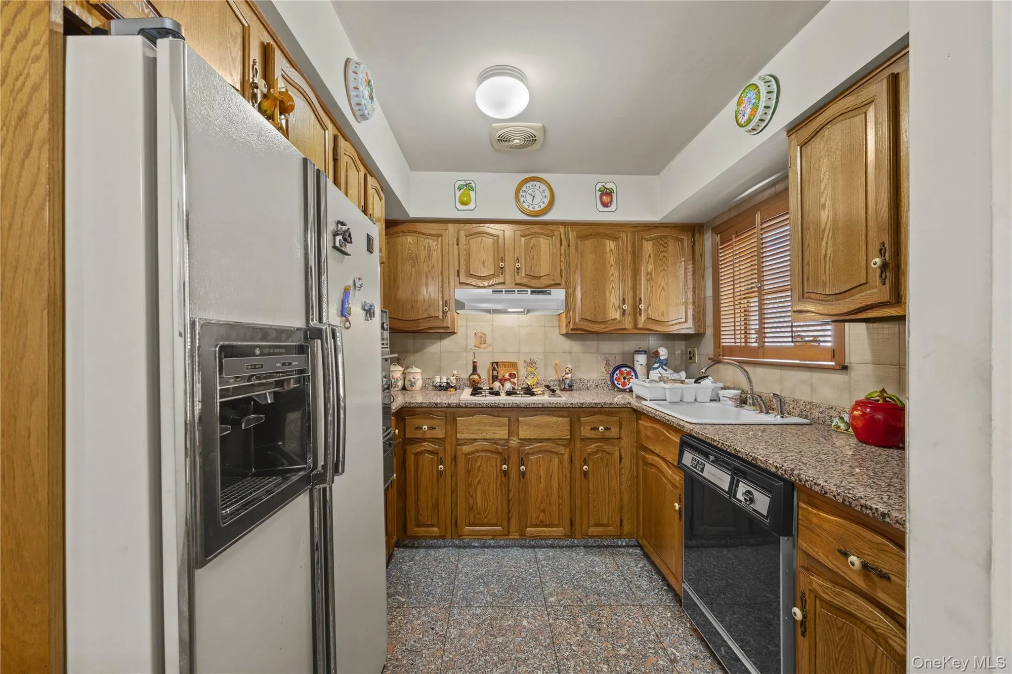 Kitchen featuring wood cabinetry, solid surface countertops, tile flooring, and a built-in dishwasher Kitchen featuring wood cabinetry, solid surface countertops, tile flooring, and a built-in dishwasher