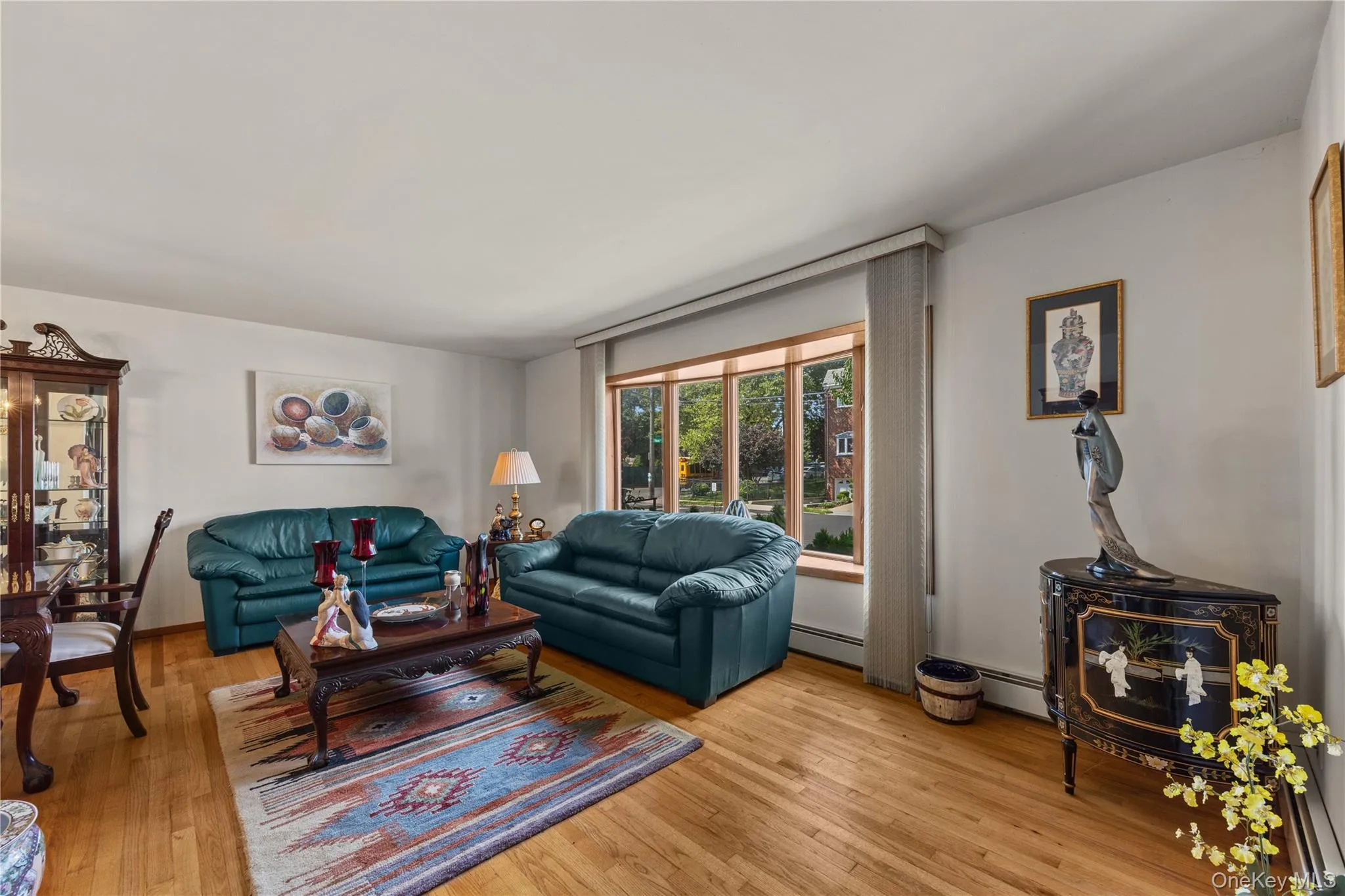 Living area featuring wood-finish flooring, a broad bay window, light neutral wall paint, and a built-in display cabinet Living area featuring wood-finish flooring, a broad bay window, light neutral wall paint, and a built-in display cabinet
