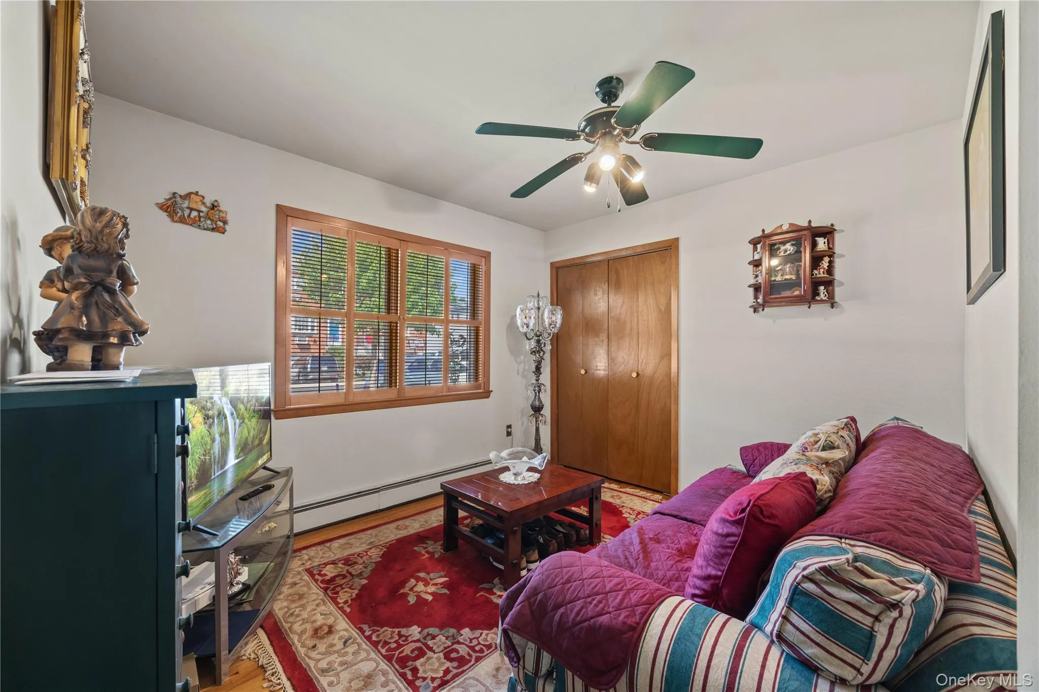 Room featuring wood-finish flooring with an area rug, a wood-framed window with horizontal blinds, and a ceiling fan with integrated lighting Room featuring wood-finish flooring with an area rug, a wood-framed window with horizontal blinds, and a ceiling fan with integrated lighting