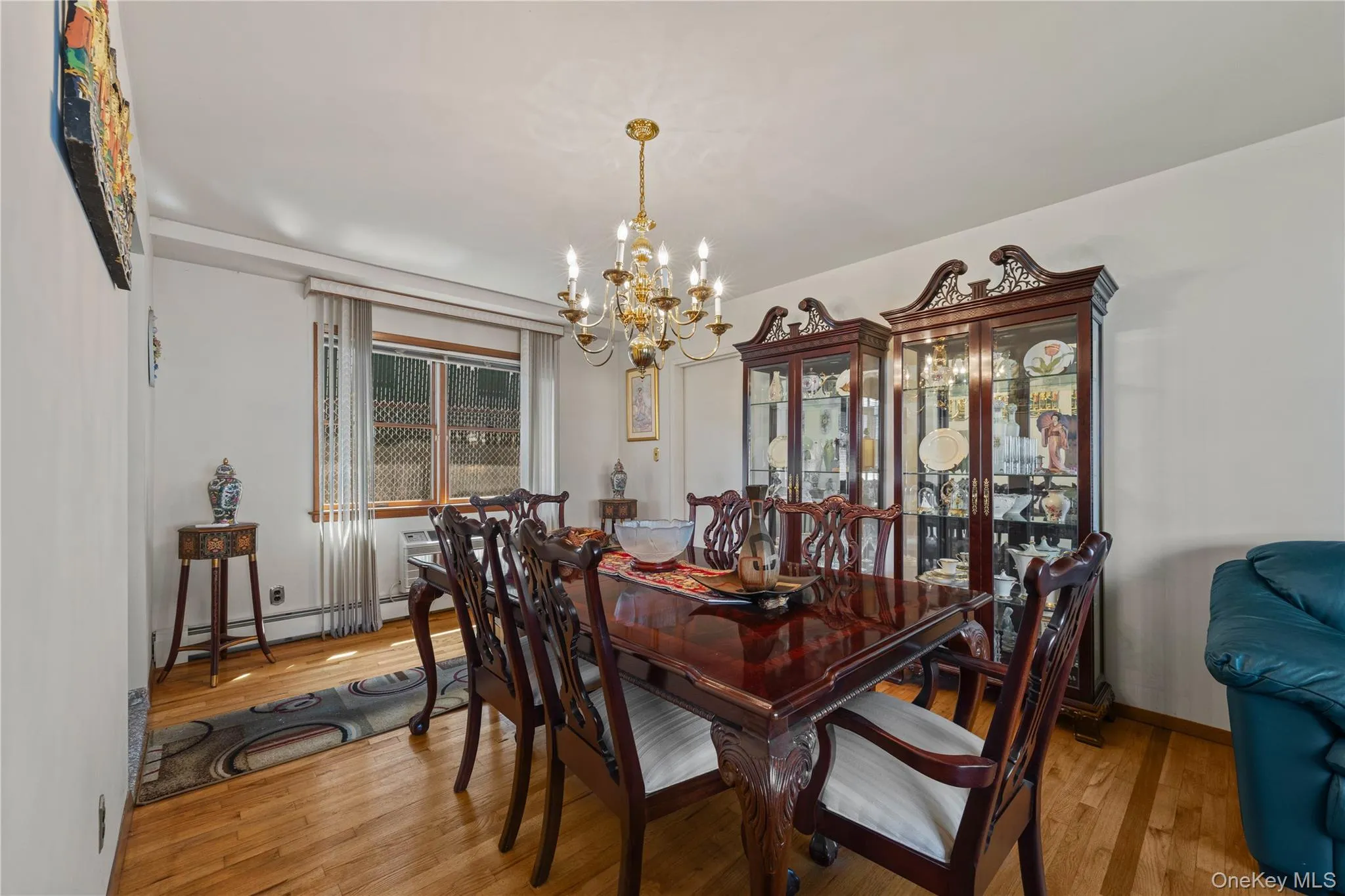 Dining area featuring wood-finish flooring, a window with horizontal blinds, and a gold-tone chandelier Dining area featuring wood-finish flooring, a window with horizontal blinds, and a gold-tone chandelier