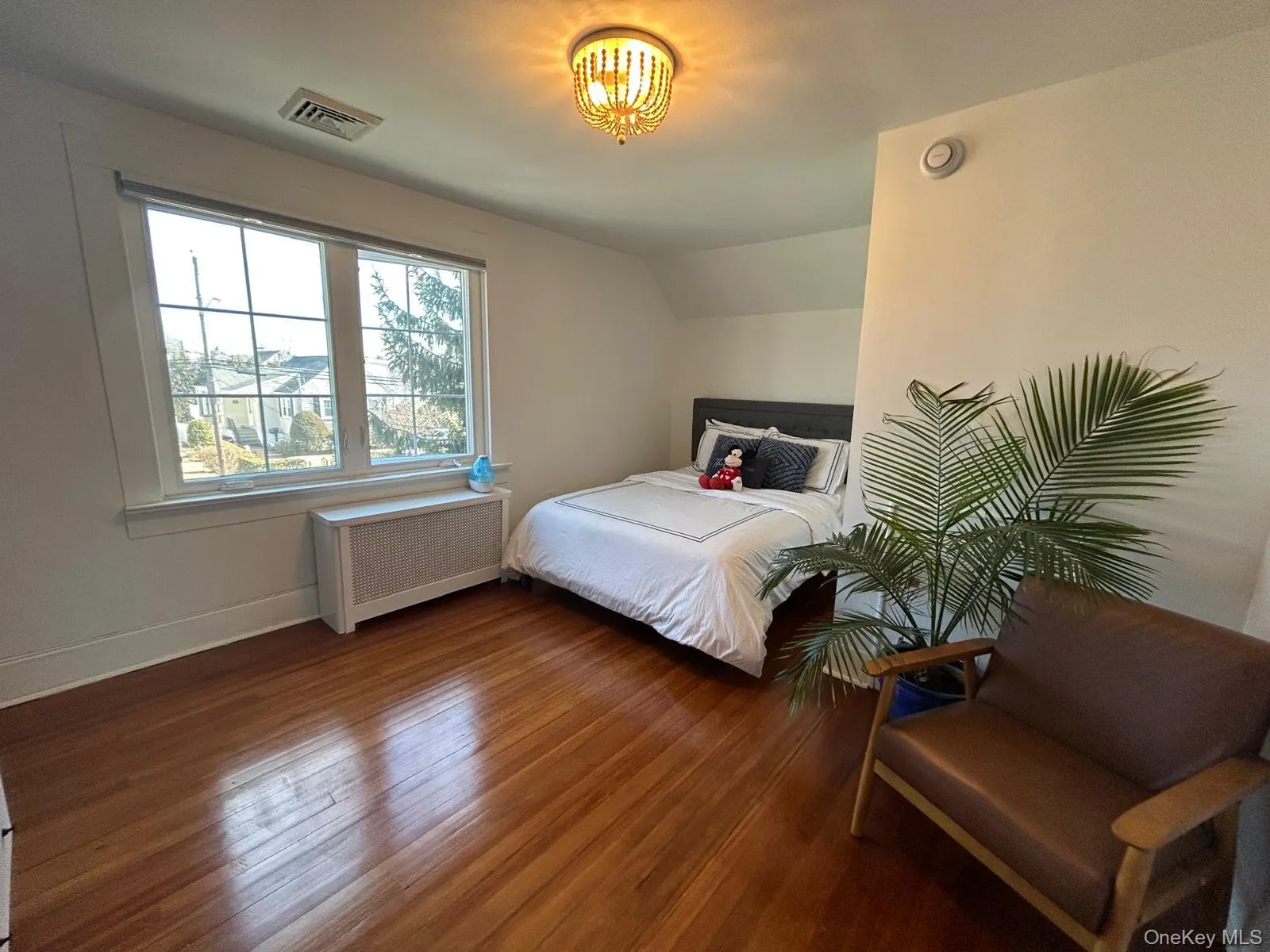 Bedroom featuring dark wood-type flooring, visible vents, baseboards, vaulted ceiling, and radiator heating unit Bedroom featuring dark wood-type flooring, visible vents, baseboards, vaulted ceiling, and radiator heating unit