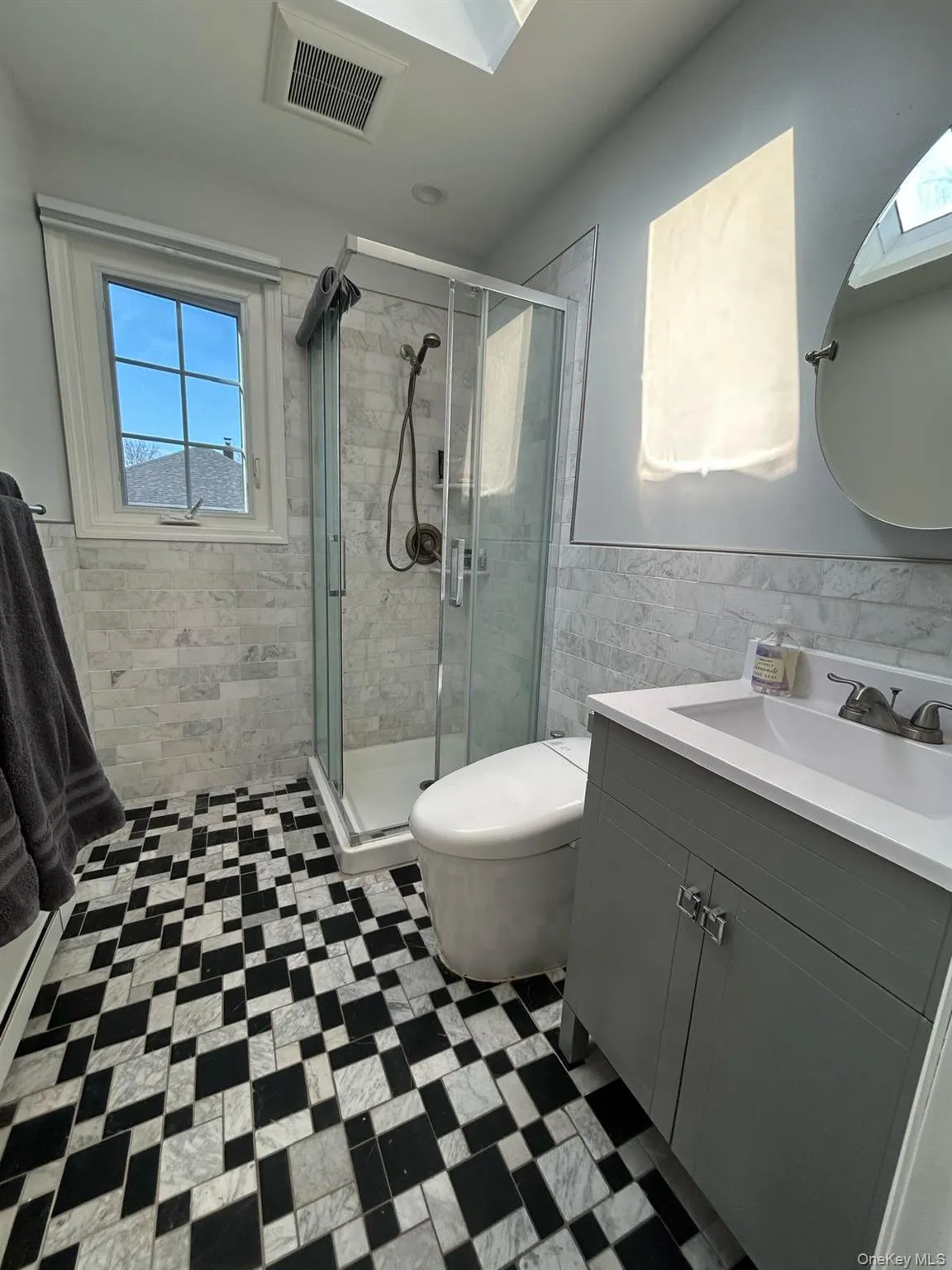 Bathroom with a skylight, visible vents, vanity, a shower stall, and tile walls Bathroom with a skylight, visible vents, vanity, a shower stall, and tile walls