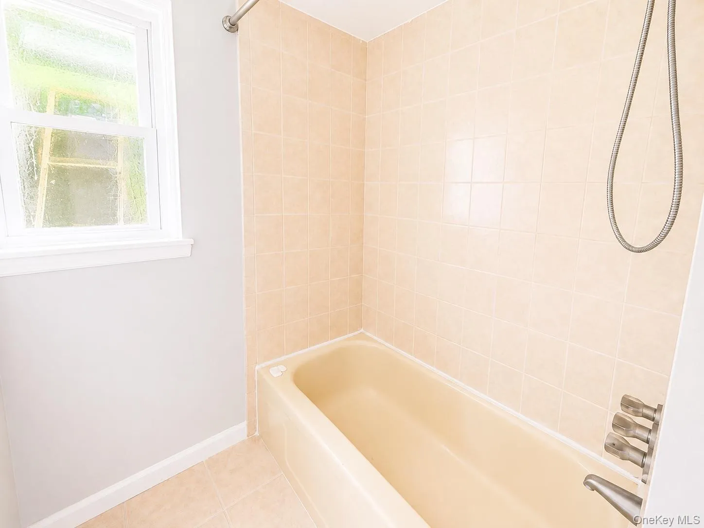 Bathtub with light-toned wall tiling, white framed window, and coordinating floor tiles Bathtub with light-toned wall tiling, white framed window, and coordinating floor tiles