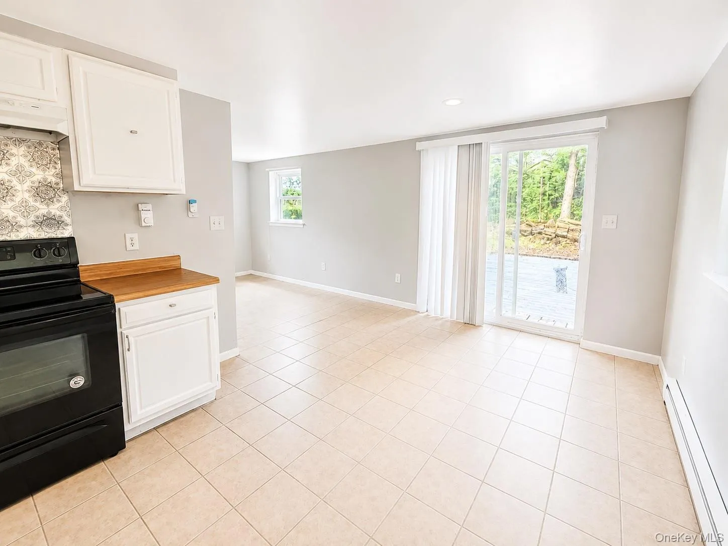 Kitchen area with white cabinetry, wood-finish countertop, and a patterned tile backsplash Kitchen area with white cabinetry, wood-finish countertop, and a patterned tile backsplash