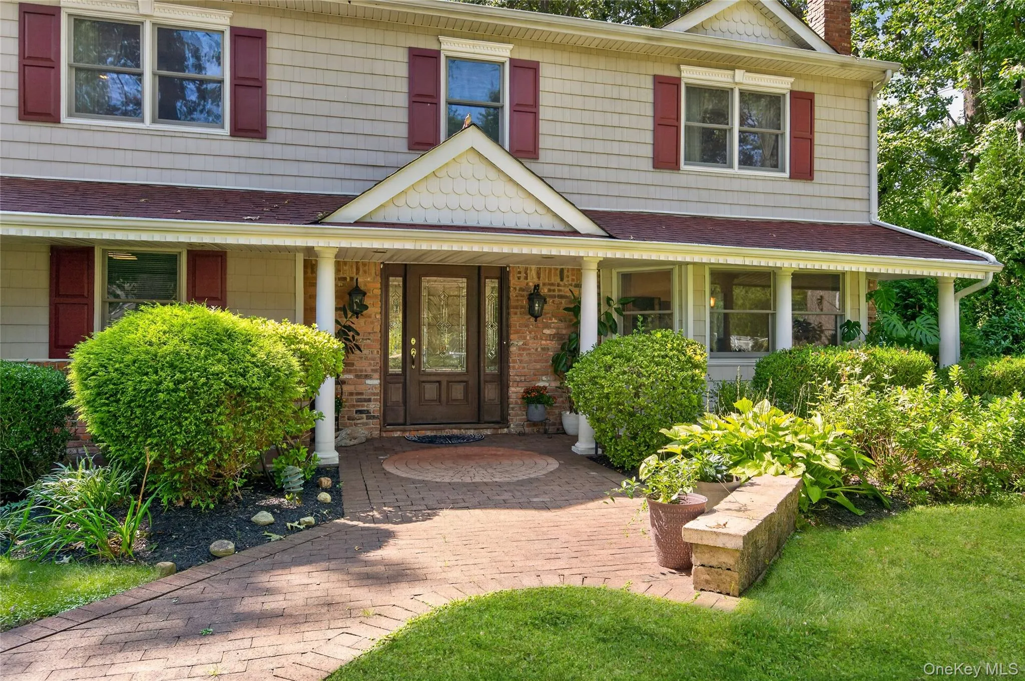 Shingle-sided exterior with red shutters, brick accents, and a covered porch Shingle-sided exterior with red shutters, brick accents, and a covered porch