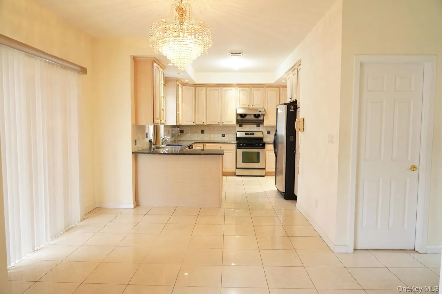 Kitchen featuring an inviting chandelier, a peninsula, under cabinet range hood, stainless steel appliances, and backsplash Kitchen featuring an inviting chandelier, a peninsula, under cabinet range hood, stainless steel appliances, and backsplash
