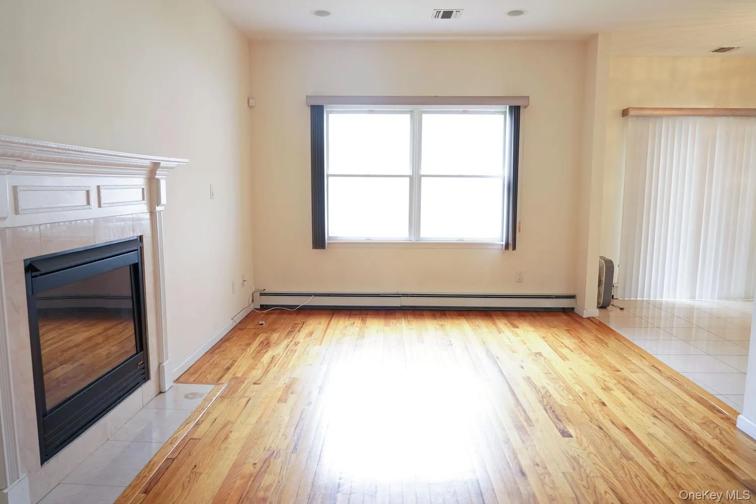 Unfurnished living room with a fireplace, light wood finished floors, baseboard heating, and visible vents Unfurnished living room with a fireplace, light wood finished floors, baseboard heating, and visible vents