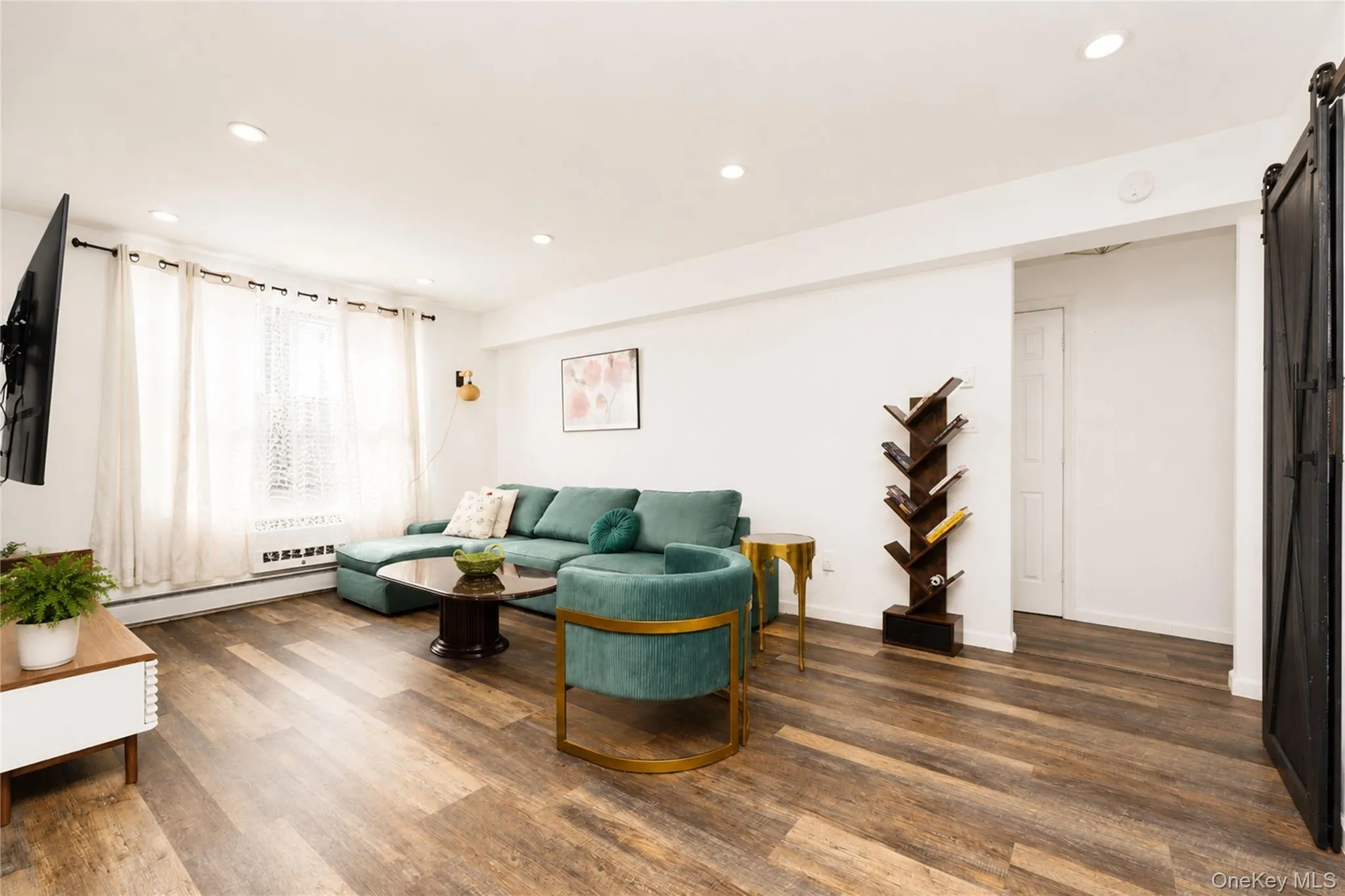 Living area featuring wood-finish flooring, recessed lighting, and a window with white curtains Living area featuring wood-finish flooring, recessed lighting, and a window with white curtains