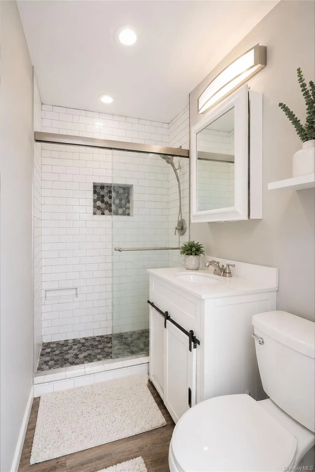 Contemporary bathroom featuring a walk-in shower with subway tile surround and hexagonal tile base, a white vanity with barn door style cabinetry, a white toilet, and recessed lighting Contemporary bathroom featuring a walk-in shower with subway tile surround and hexagonal tile base, a white vanity with barn door style cabinetry, a white toilet, and recessed lighting
