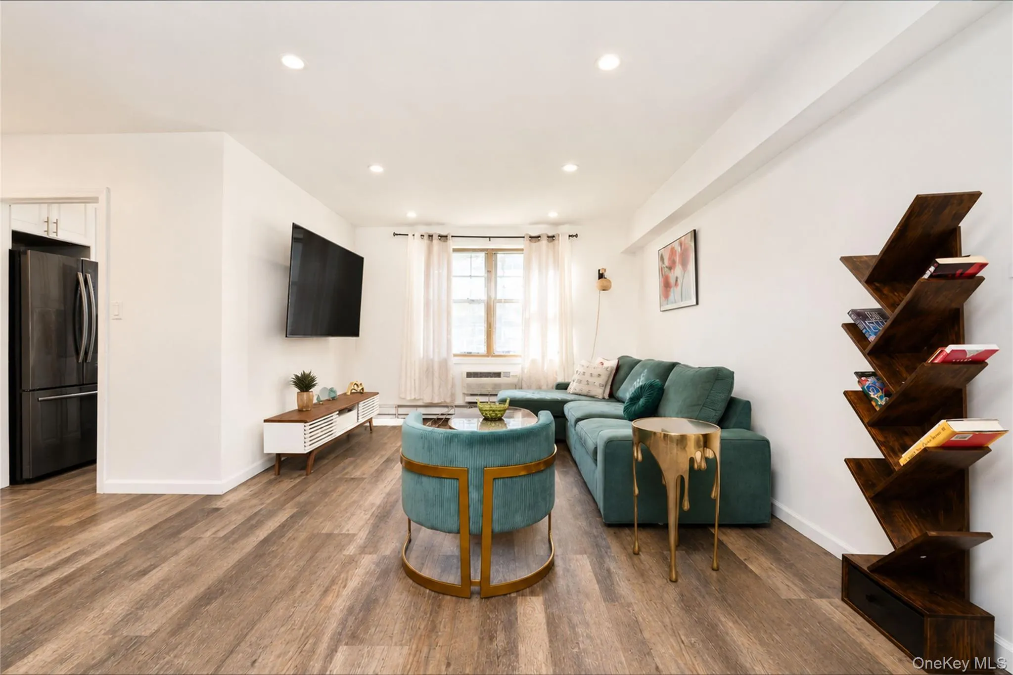 Spacious living area featuring wood-finish flooring, white walls, and recessed lighting Spacious living area featuring wood-finish flooring, white walls, and recessed lighting