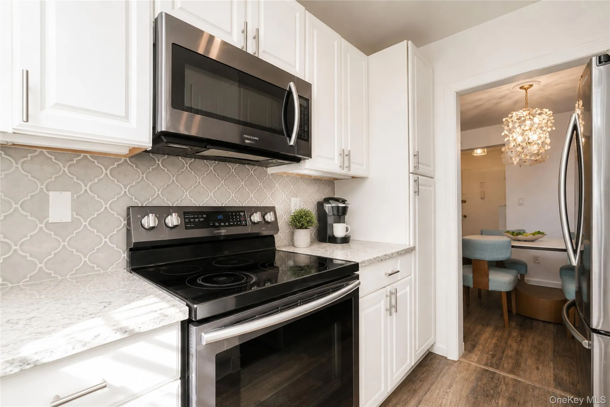 Kitchen featuring white cabinetry, stainless steel appliances, patterned tile backsplash, and light-colored countertops Kitchen featuring white cabinetry, stainless steel appliances, patterned tile backsplash, and light-colored countertops