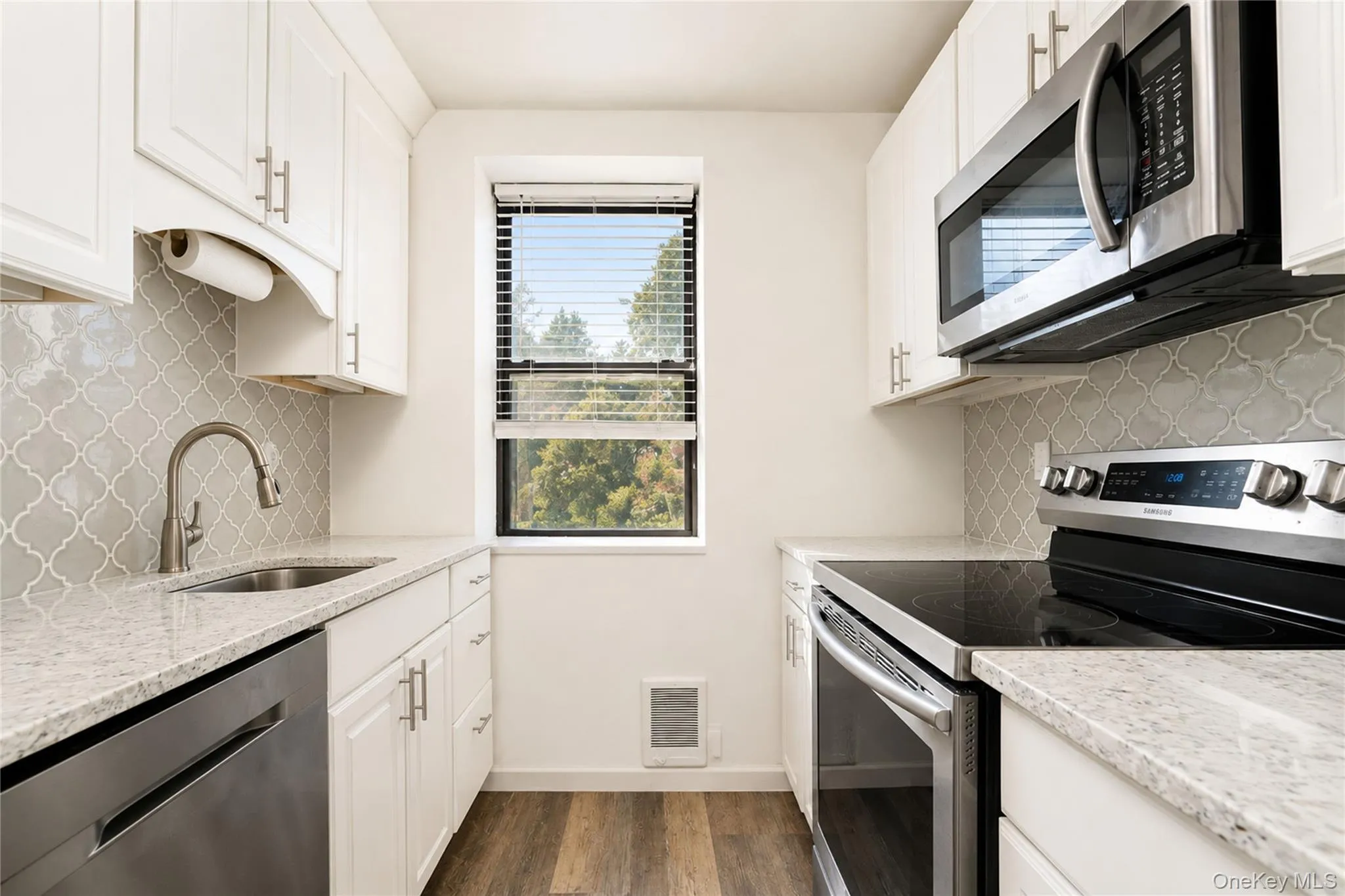 Kitchen featuring white cabinetry, light-toned countertops, a patterned backsplash, and stainless steel appliances including a built-in microwave and electric range Kitchen featuring white cabinetry, light-toned countertops, a patterned backsplash, and stainless steel appliances including a built-in microwave and electric range