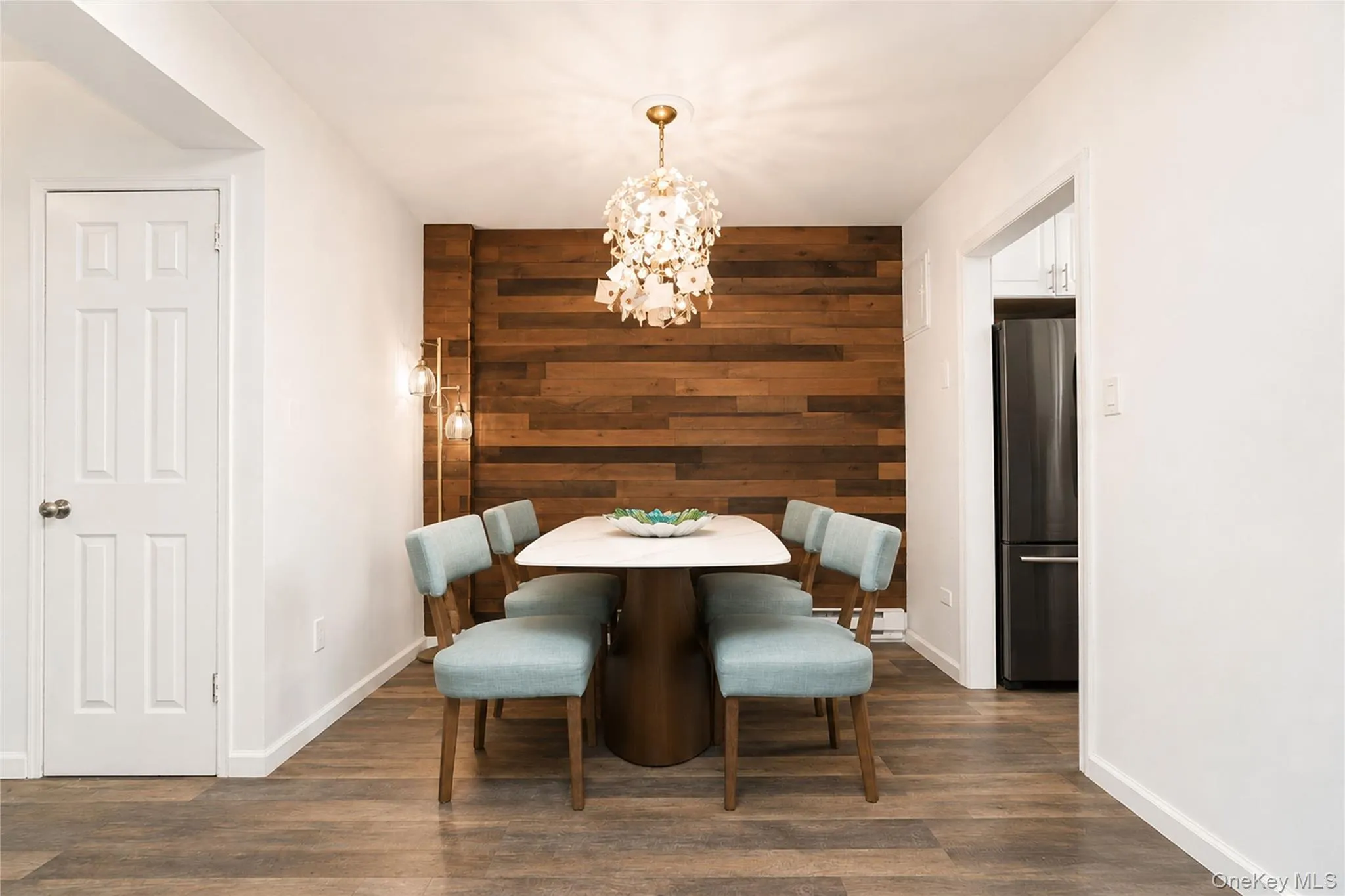 Dining area featuring a wood-panel accent wall, wood-finish flooring, and a decorative chandelier Dining area featuring a wood-panel accent wall, wood-finish flooring, and a decorative chandelier