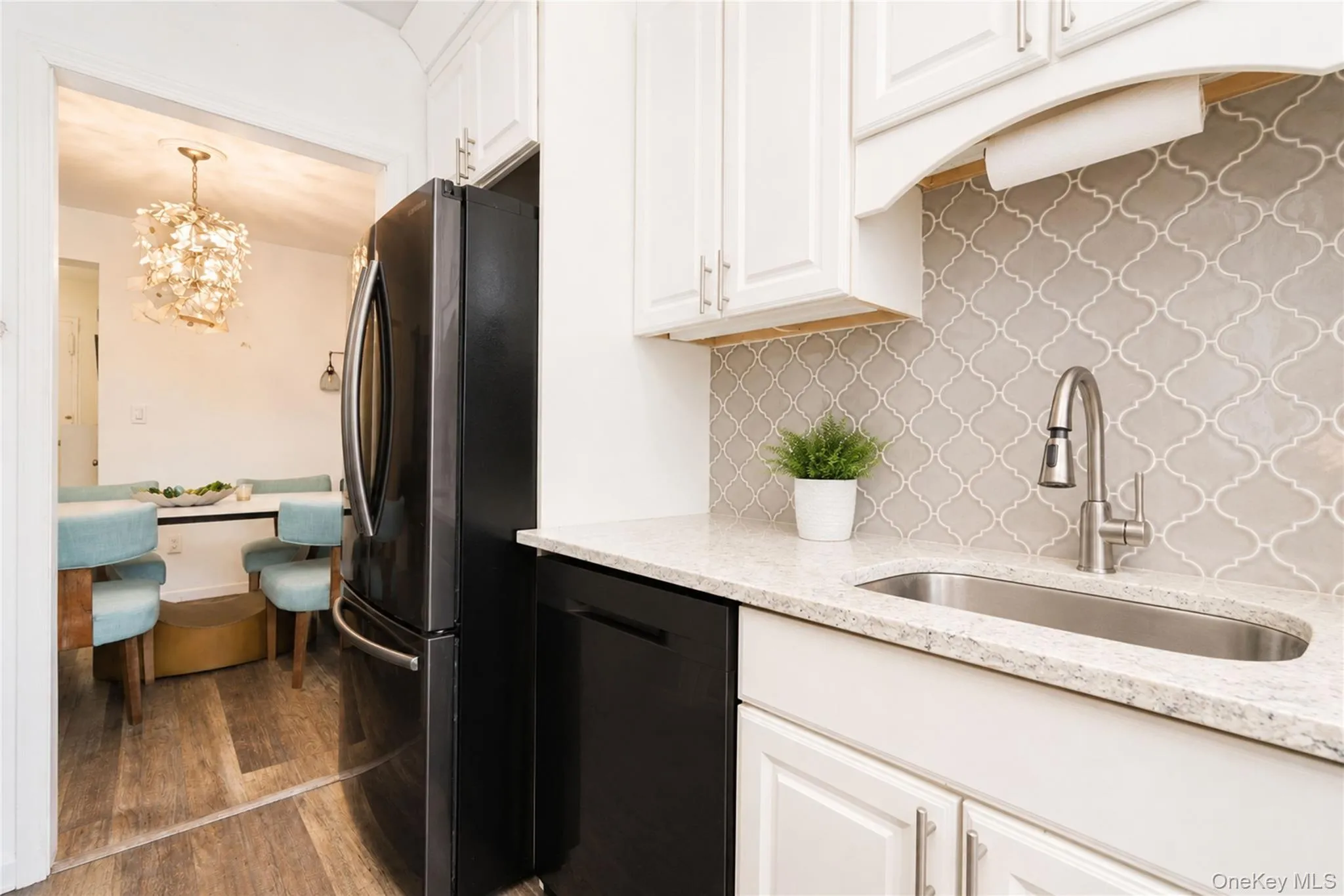 Modern kitchen featuring white cabinetry, granite-style countertops, stainless steel sink, and a decorative tile backsplash Modern kitchen featuring white cabinetry, granite-style countertops, stainless steel sink, and a decorative tile backsplash